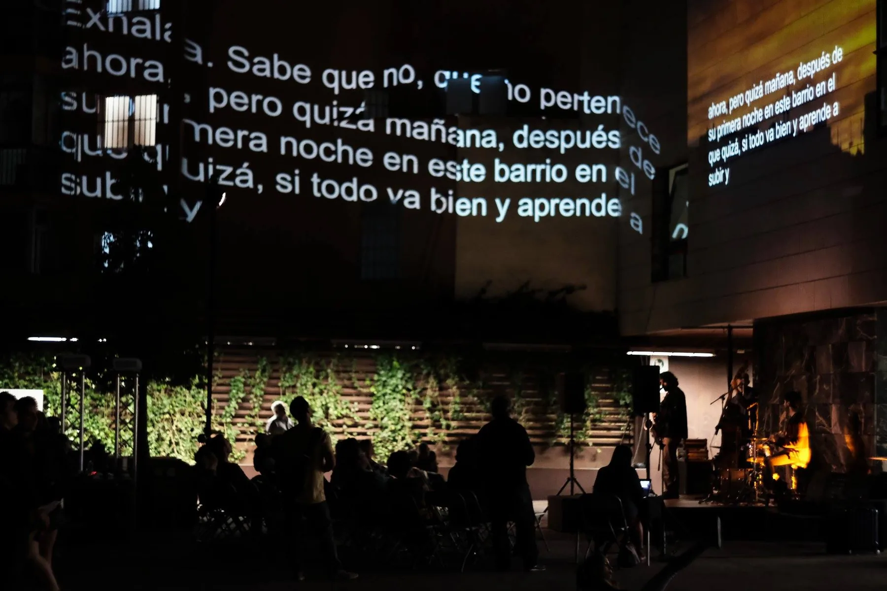 Texto proyectado sobre las fachadas de una plaza, con público y banda en directo, El Carmel, Barcelona, 2019